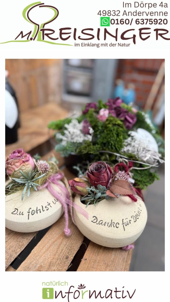 Zwei dekorative Steine mit Schriftzügen "Du fehlst mir" und "Danke für Dein", umgeben von Trockenblumen in rosa und lila Farbtönen, vor einem botanischen Arrangement mit grünen Pflanzen und weiteren Blüten.