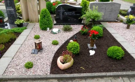 Gräberfeld mit liebevoll gestalteten Grabsteinen und bepflanzten Beeten. Eine Mischung aus bunten Blumen, Sträuchern und dekorativen Elementen wie Laternen und Steinen verleiht dem Ort eine ruhige und respektvolle Atmosphäre. Der Grabstein ist mit einer Inschrift versehen und von einer gepflegten Landschaft umgeben.