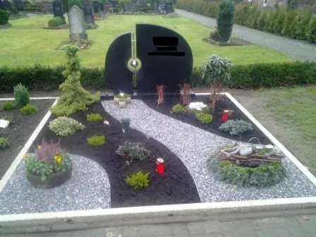 Eine gepflegte Grabstätte mit modernen Elementen, geschwungenen Wegen und verschiedenen Pflanzenarten, umgeben von Grabsteinen.